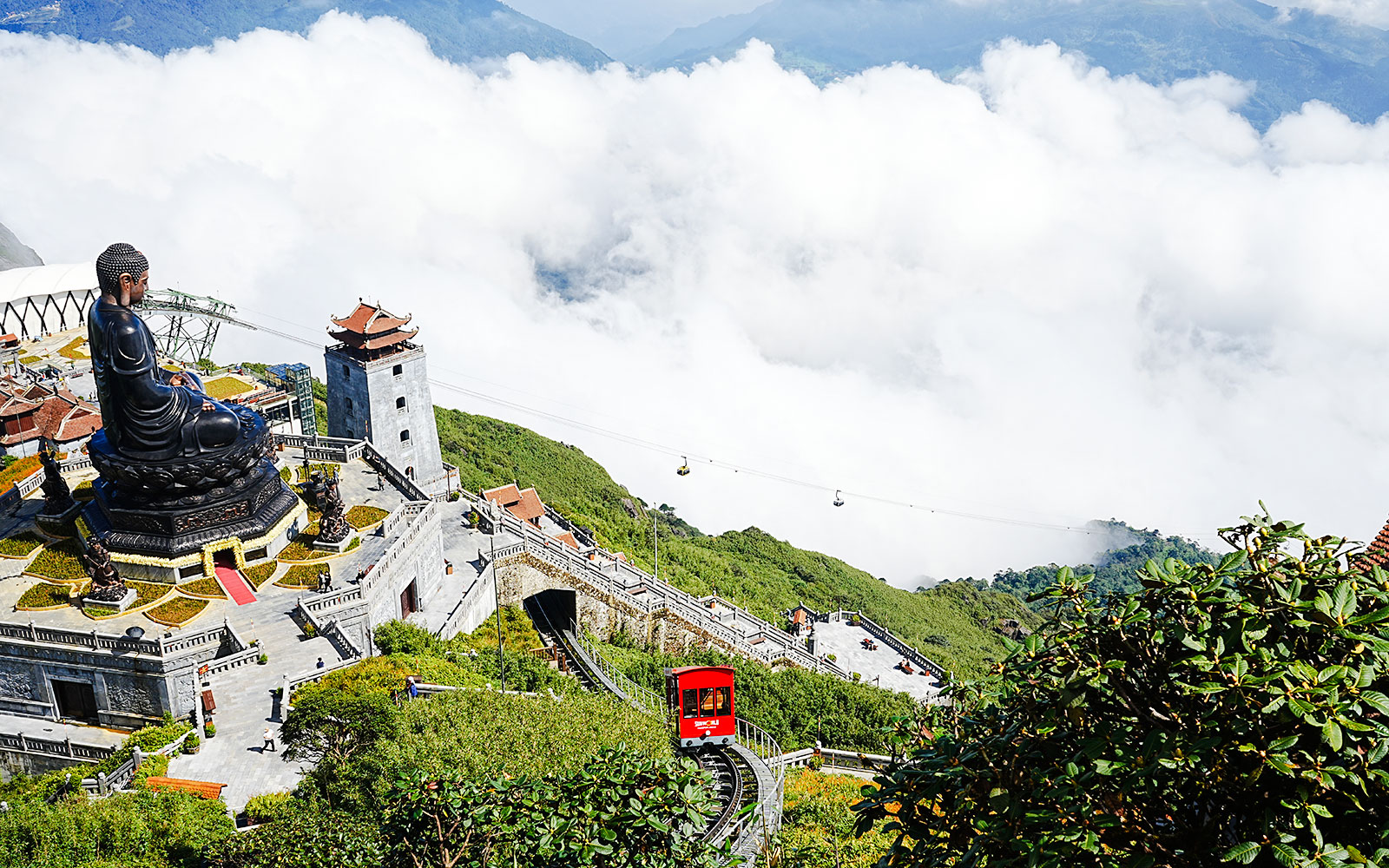 Fansipan Mountain cable car and large Buddha statue amidst clouds and greenery.