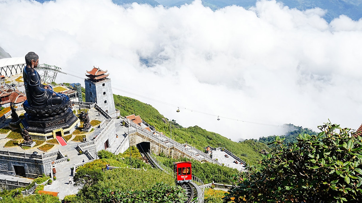 Fansipan Mountain cable car and large Buddha statue amidst clouds and greenery.