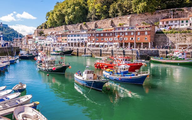 Colorful fishing boats docked in Hondarribia harbor, Spain, with historic buildings in the background.