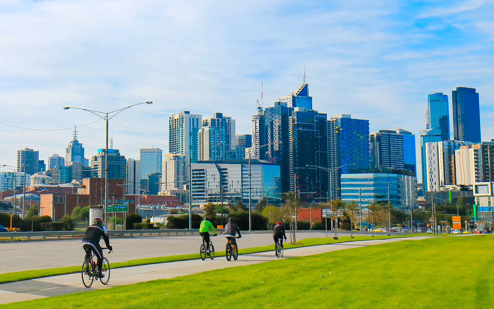 Cyclists riding along a path with Melbourne skyline in the background.