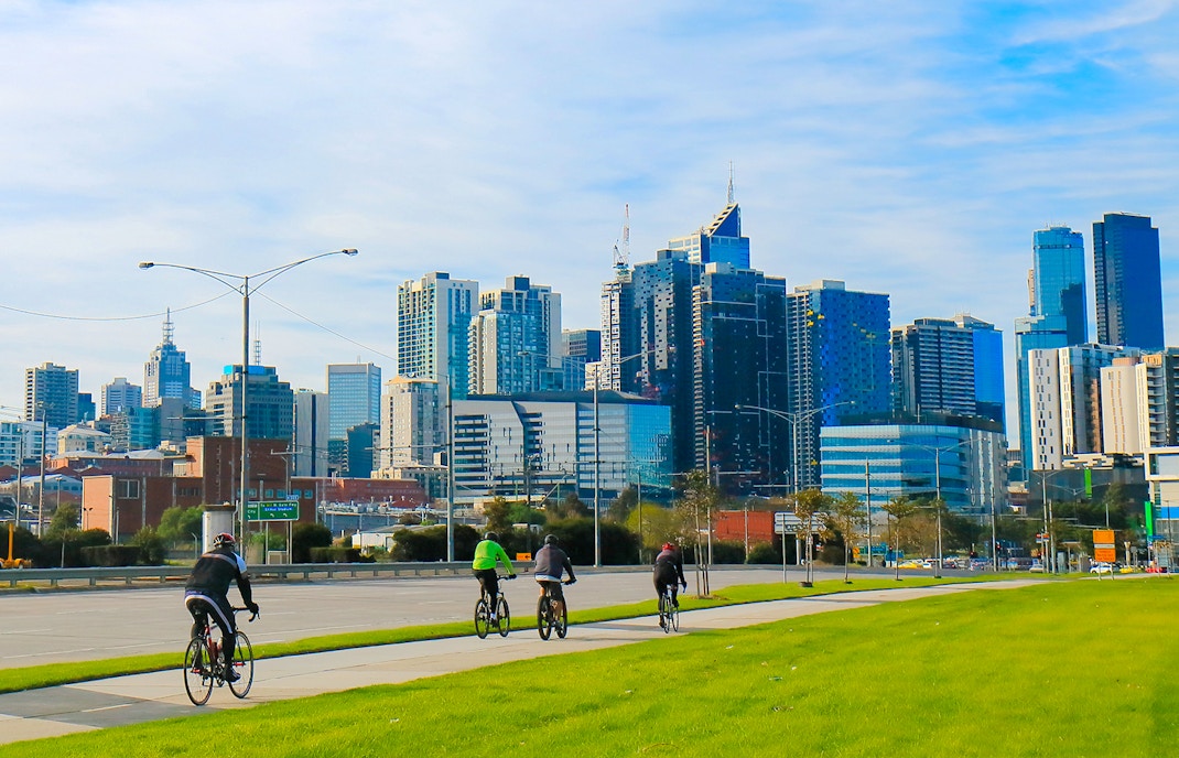 Cyclists riding along a path with Melbourne skyline in the background.