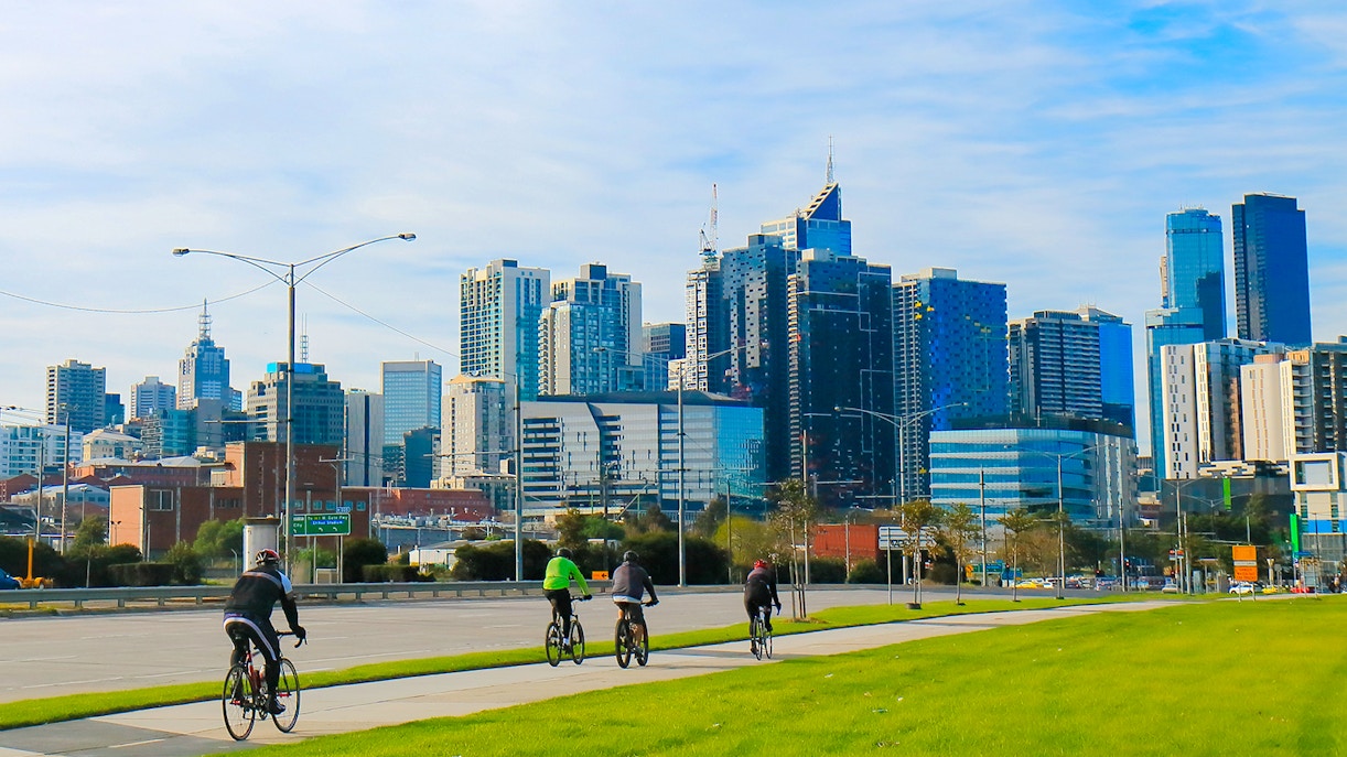 Cyclists riding along a path with Melbourne skyline in the background.