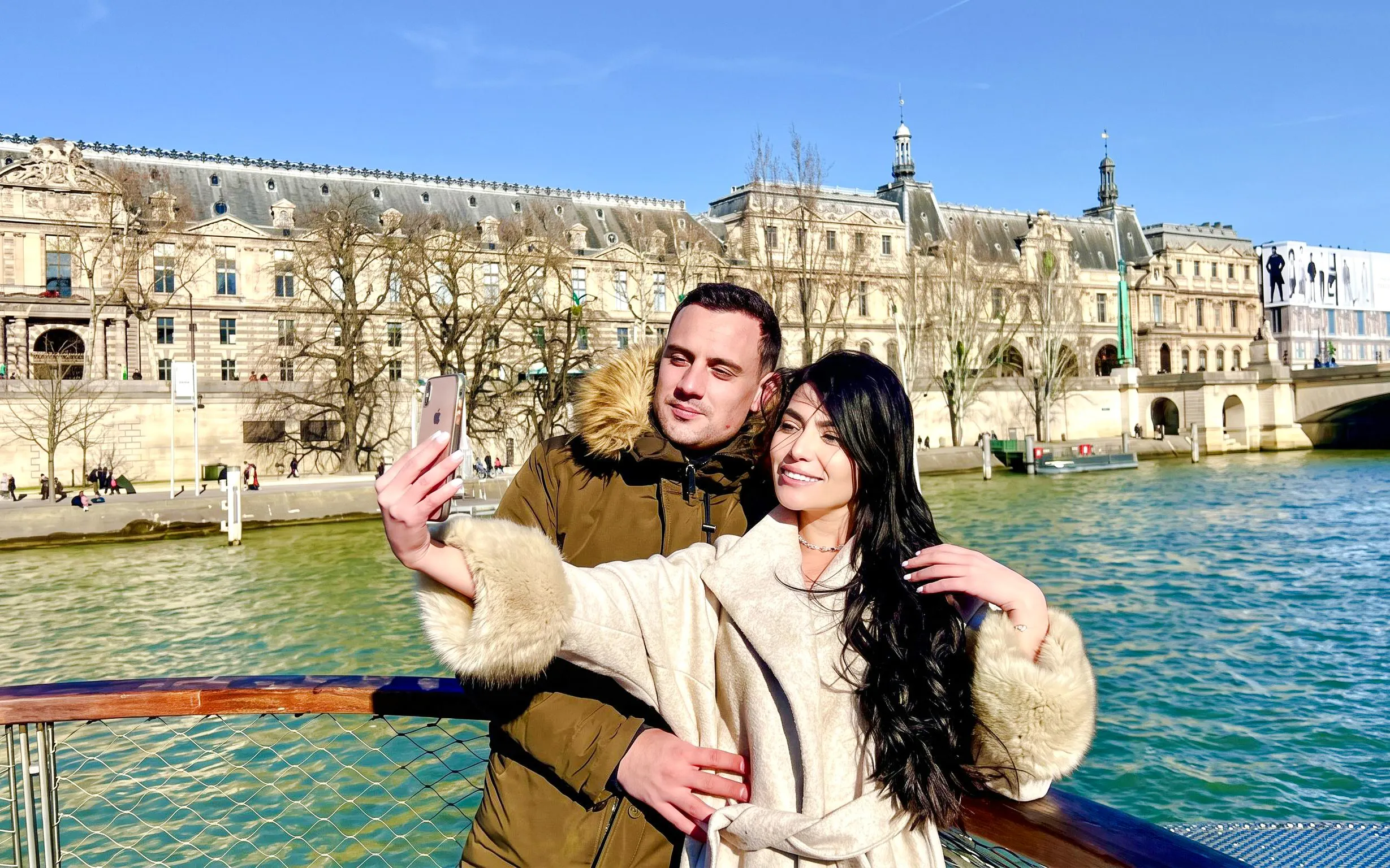 Couple taking a selfie on a Seine River cruise with Parisian architecture in the background.