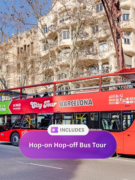 Red double-decker bus on a hop-on hop-off tour in front of Casa Milà, Barcelona.
