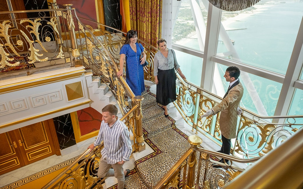 Guests touring Burj Al Arab's ornate staircase with views of Dubai coastline.