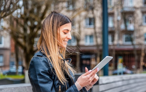 Woman using a tablet outdoors in a city setting.