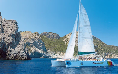 Catamaran sailing near rocky cliffs in Alcudia, Mallorca.