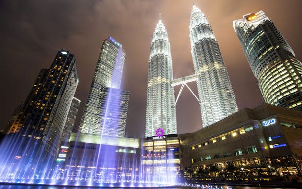 PETRONAS Twin Towers illuminated at night with surrounding skyscrapers in Kuala Lumpur.