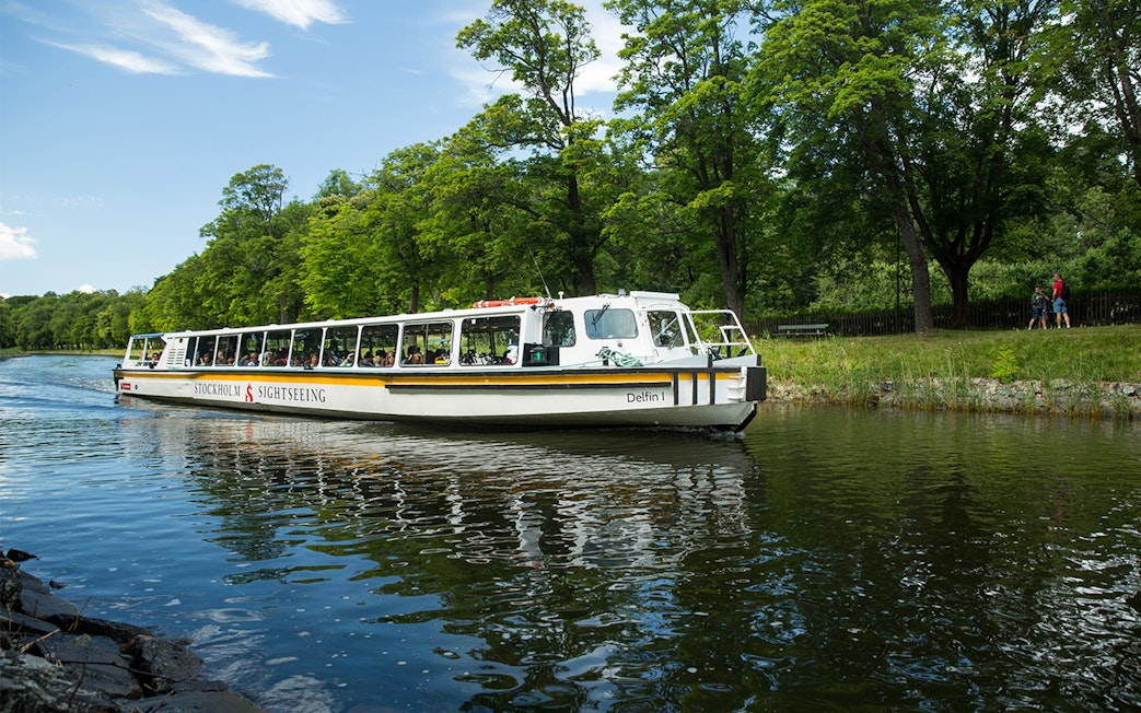 Stockholm sightseeing boat on a canal surrounded by lush greenery.