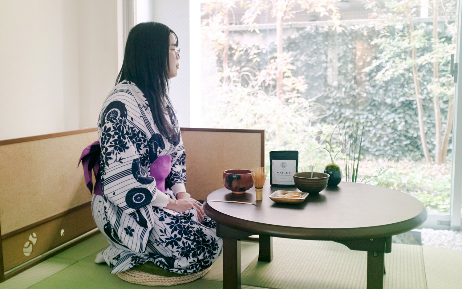 Person in kimono seated at a table with matcha tea set in a traditional Tokyo setting.