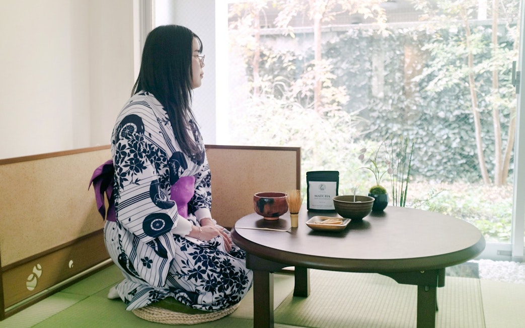 Person in kimono seated at a table with matcha tea set in a traditional Tokyo setting.