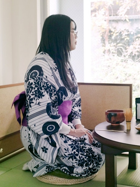 Person in kimono seated at a table with matcha tea set in a traditional Tokyo setting.