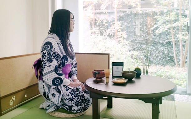 Person in kimono seated at a table with matcha tea set in a traditional Tokyo setting.