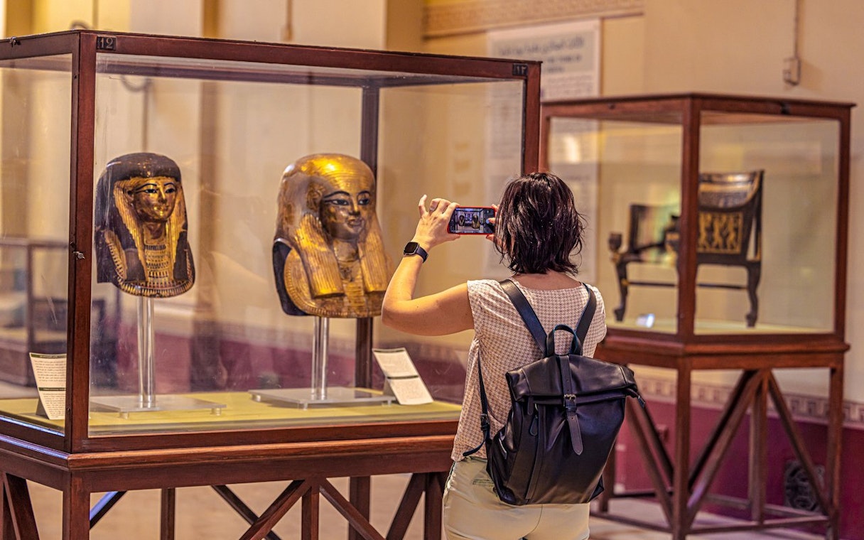 Visitor photographing ancient Egyptian masks at the Grand Egyptian Museum.