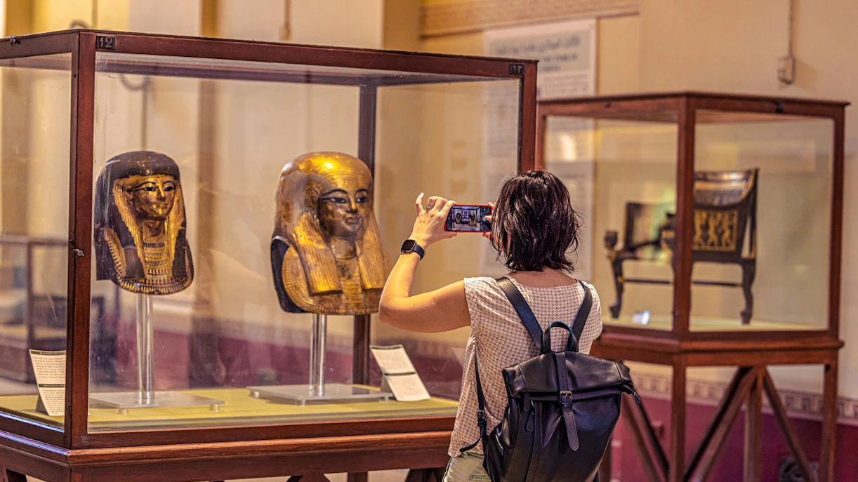 Visitor photographing ancient Egyptian masks at the Grand Egyptian Museum.