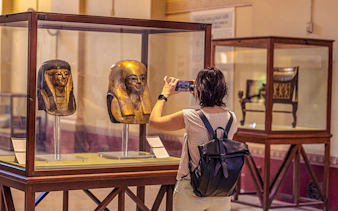 Visitor photographing ancient Egyptian masks at the Grand Egyptian Museum.