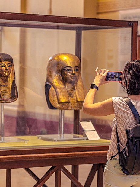 Visitor photographing ancient Egyptian masks at the Grand Egyptian Museum.