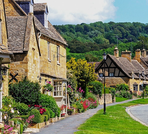 Cotswold village street with stone cottages and colorful gardens, England.