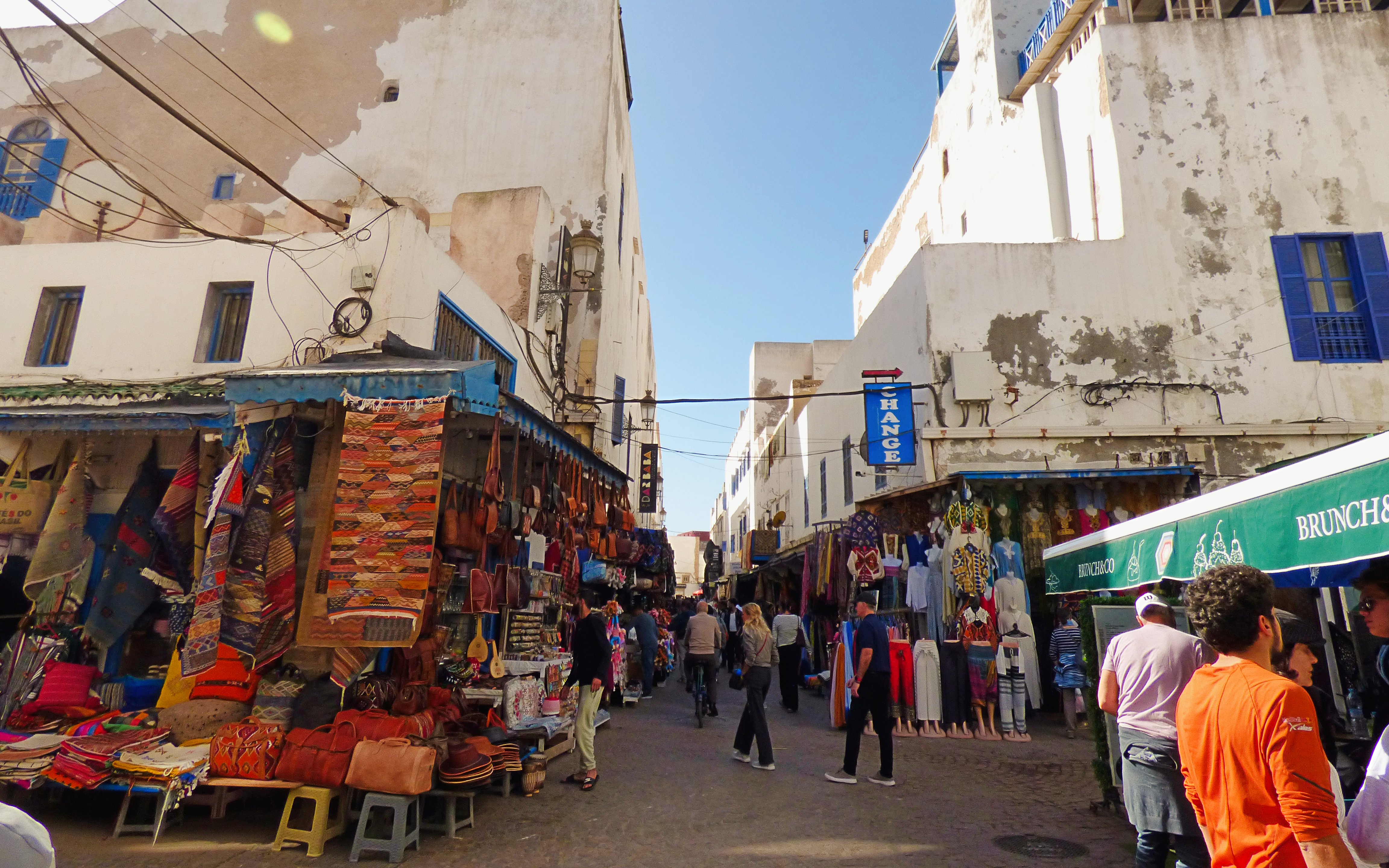 Essaouira market street with colorful textiles and leather goods displayed.