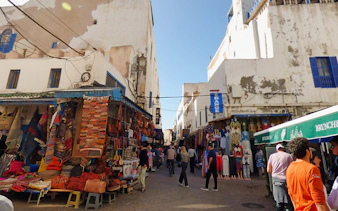 Essaouira market street with colorful textiles and leather goods displayed.