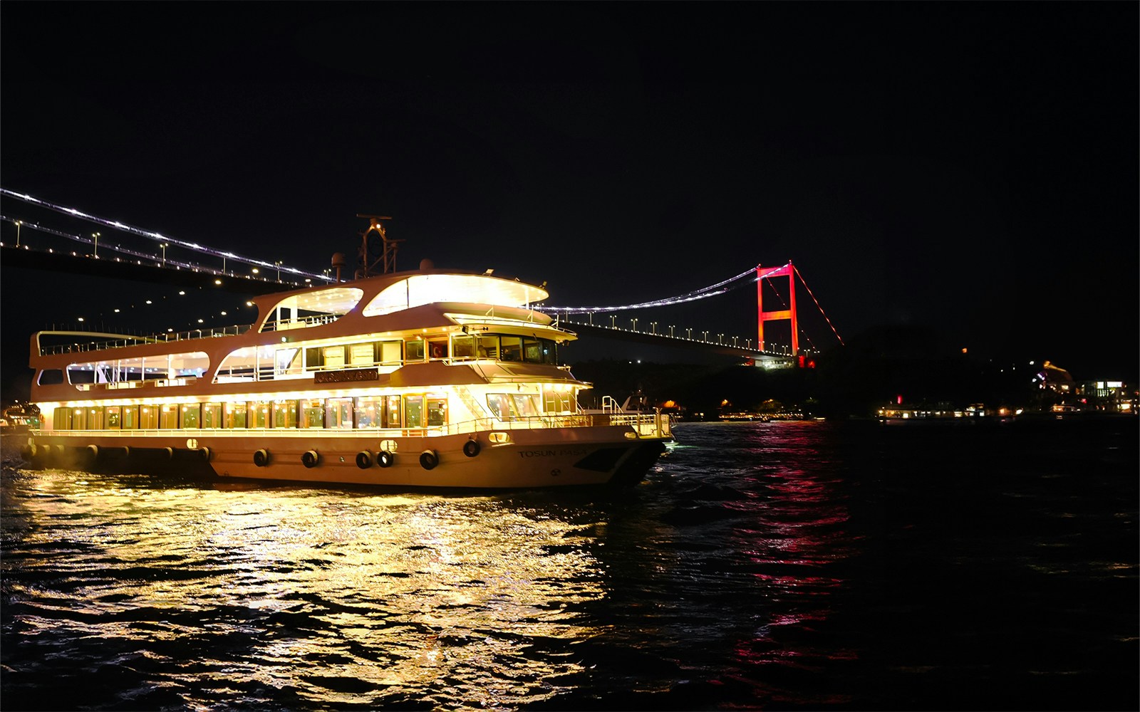 Bosphorus dinner cruise with Turkish show, Istanbul skyline and illuminated bridge in background.