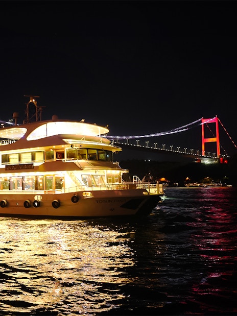 Bosphorus dinner cruise ship illuminated at night with bridge in Istanbul.