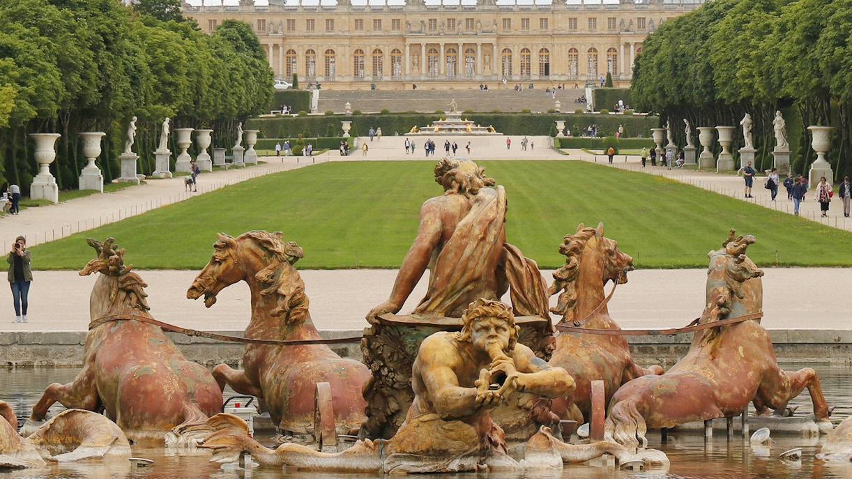 Fountain of Apollo in the gardens of Versailles, France with palace in background.