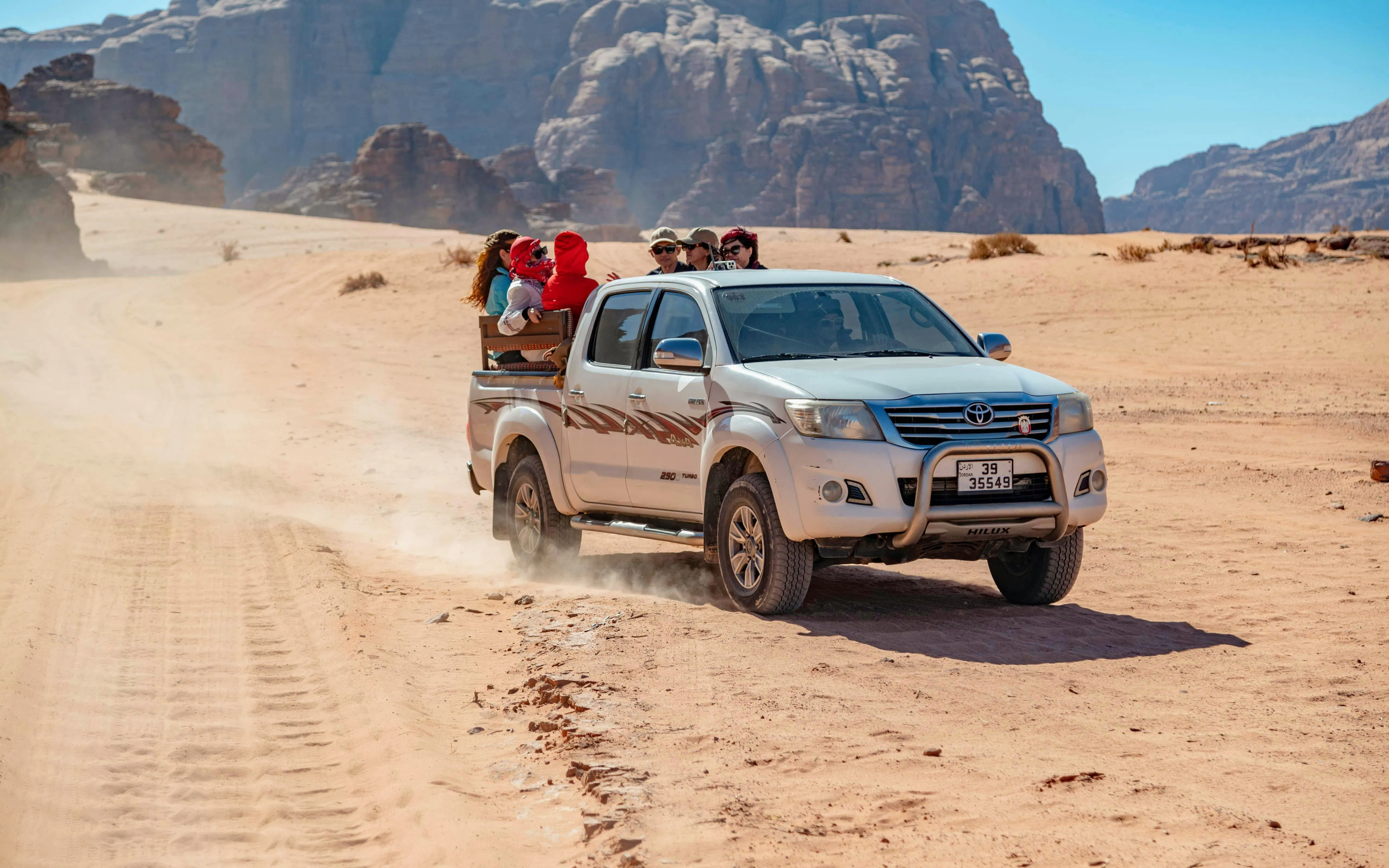 Tourists in a pickup truck exploring the desert landscape of Wadi Rum, Jordan.