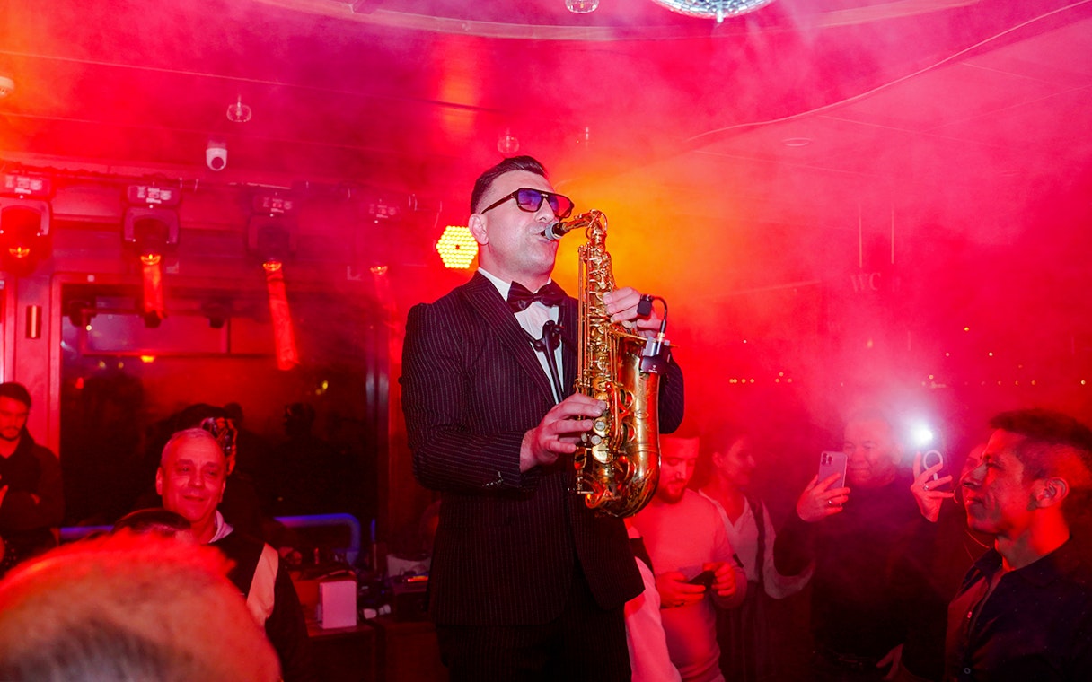 Saxophonist performing on Bosphorus dinner cruise with audience in background.