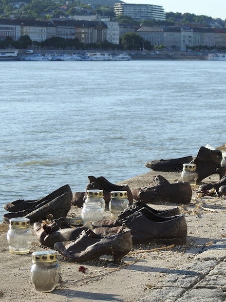 Shoes Memorial on the Danube Riverbank in Budapest, Hungary, with candles and cityscape in background.