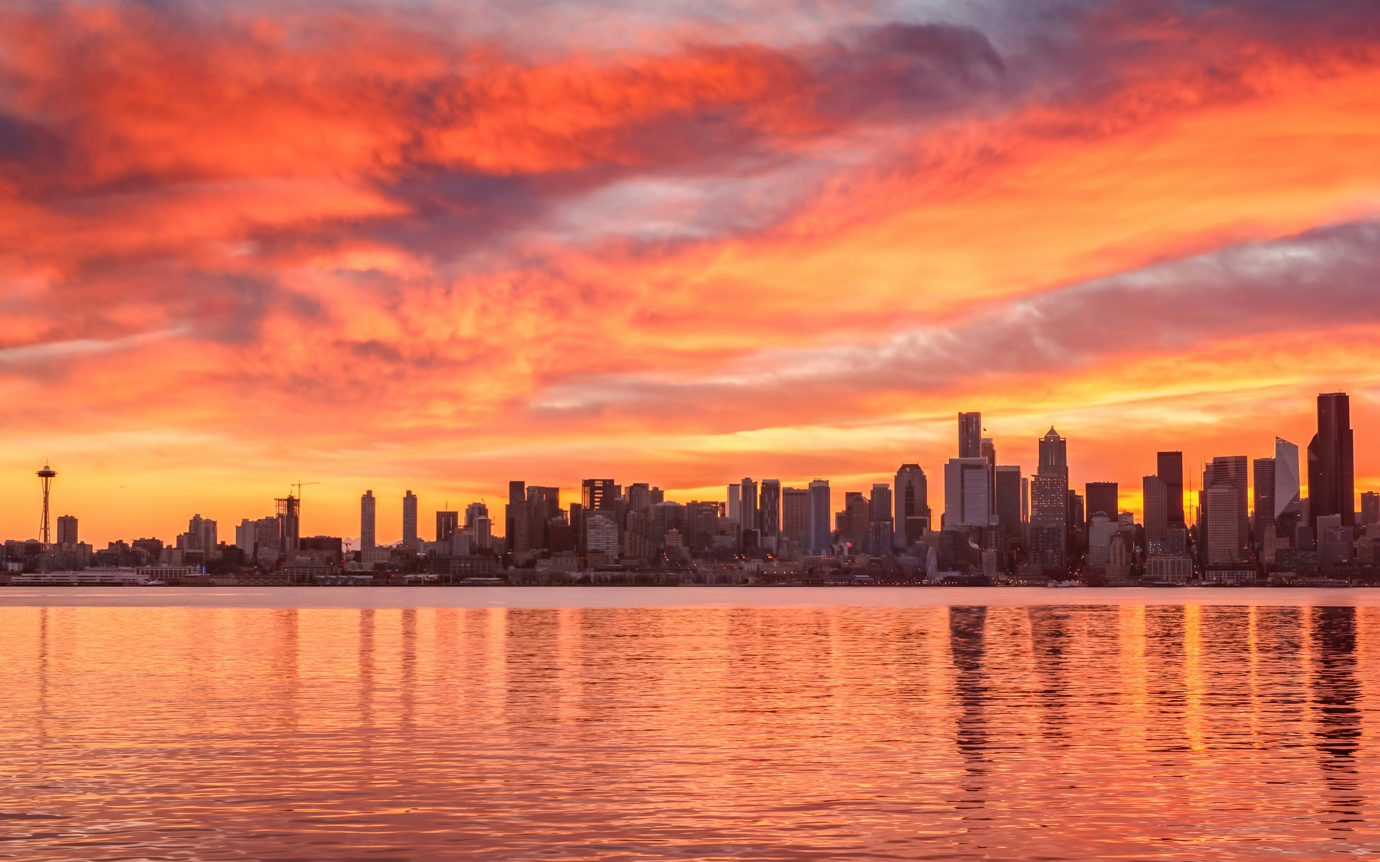 Seattle downtown skyline at sunrise with vibrant orange sky reflecting on water.