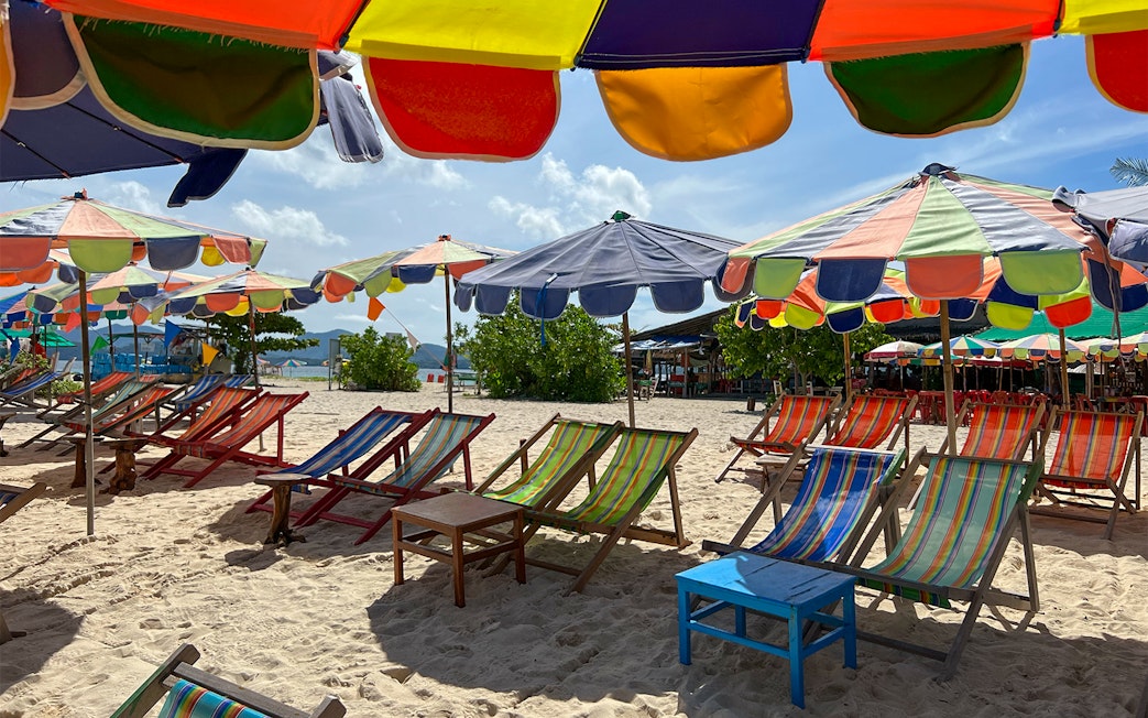 Colorful beach umbrellas and chairs on sand in Khai Island.