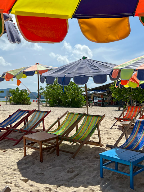 Colorful beach umbrellas and chairs on sand in Khai Island.
