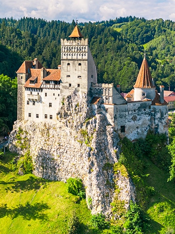 Bran Castle in Bucharest surrounded by lush green hills and forest.