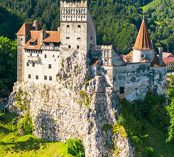 Bran Castle in Bucharest surrounded by lush green hills and forest.