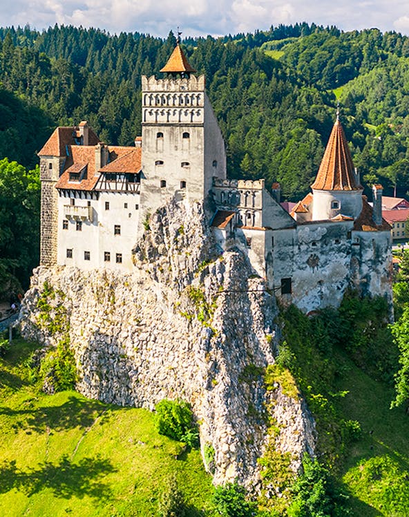 Bran Castle in Bucharest surrounded by lush green hills and forest.