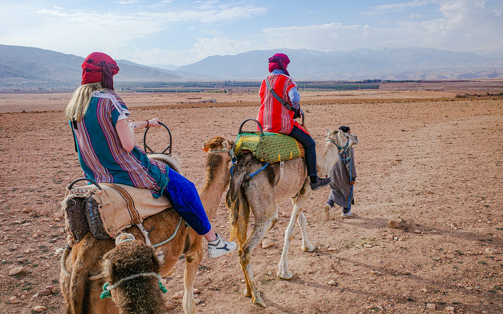 Tourists riding camels in Agafay Desert, Morocco with distant mountains.