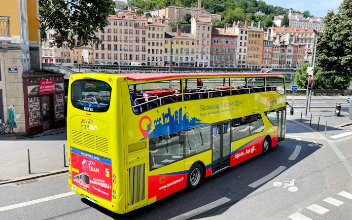 Open-top Lyon city tour bus on street with historic buildings in background, France.