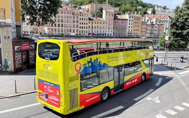 Open-top Lyon city tour bus on street with historic buildings in background, France.