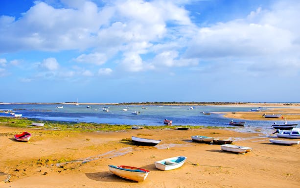 Boats on sandy shore of Ria Formosa lagoon under blue sky.