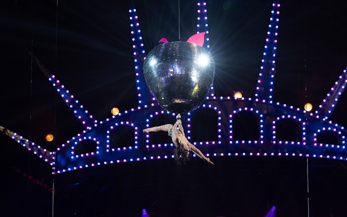Performer hanging from a disco ball in Mad Apple show.