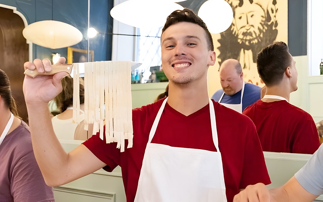 Cooking class participant holding fresh fettuccine in Rome near Piazza Navona.