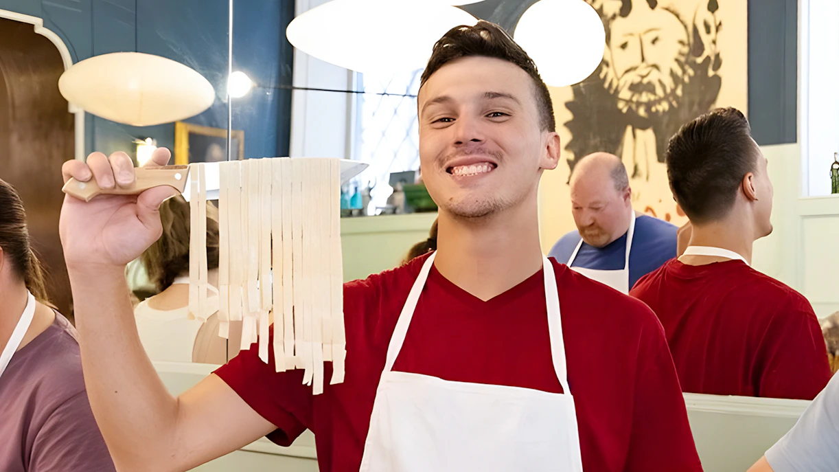 Cooking class participant holding fresh fettuccine in Rome near Piazza Navona.