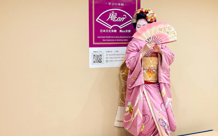 Maiko in pink kimono holding a traditional Japanese fan in Kyoto.