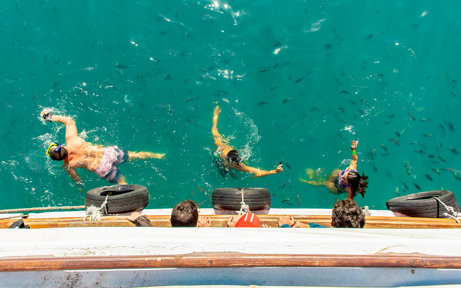 People snorkeling with fish near a boat in Blue Lagoon, Ilha Grande, Brazil.