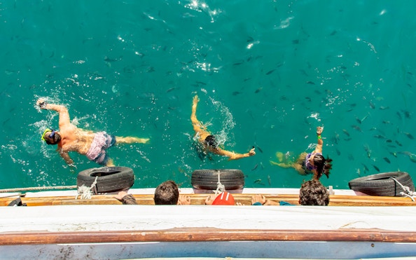 People snorkeling with fish near a boat in Blue Lagoon, Ilha Grande, Brazil.