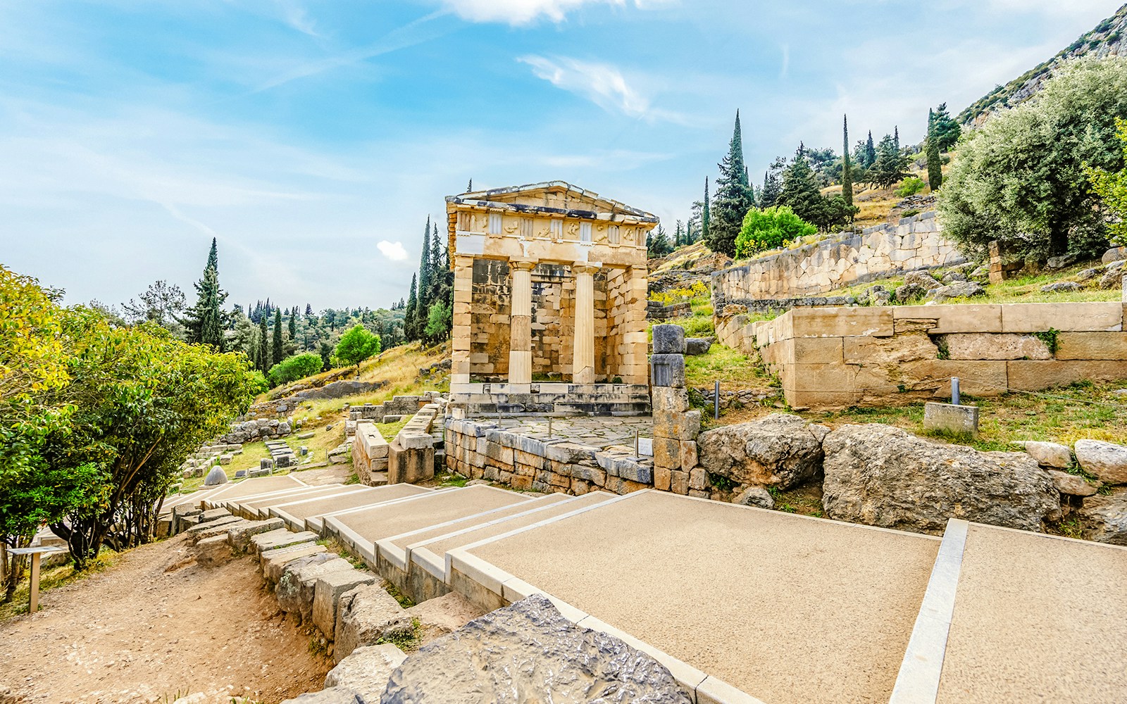 Athenian Treasury at Delphi with surrounding ancient ruins and landscape.