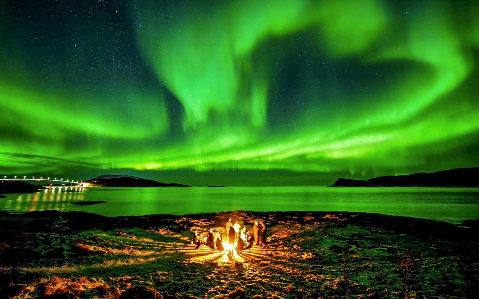 Guests gathered around a campfire under Northern Lights near Tromsø, Norway.