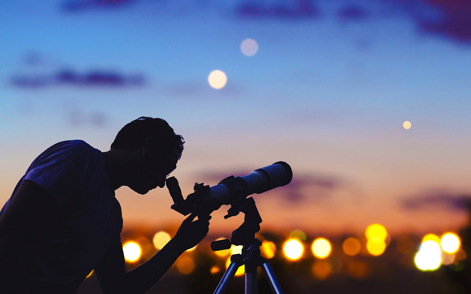 Astronomer using telescope to observe stars and Moon in a clear night sky.