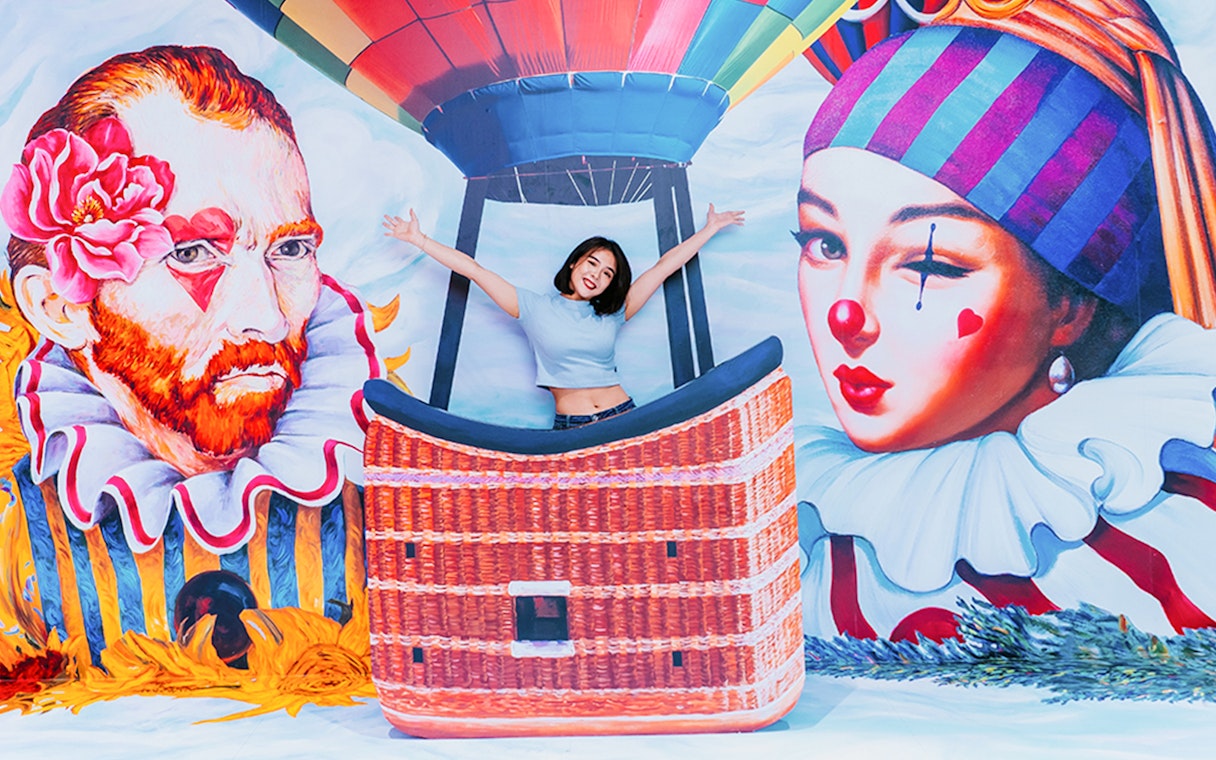 Woman posing in front of colorful mural with hot air balloon, Singapore Cable Car Flexi Pass.